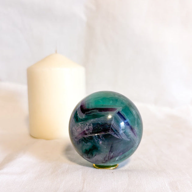 Fluorite crystal sphere on a white surface with a candle in the background