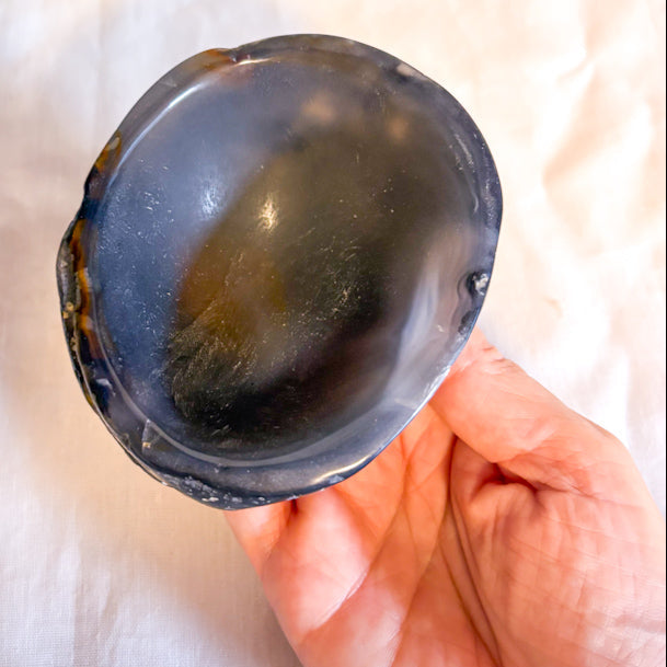 Person holding a dark-colored crystal bowl on a white fabric background