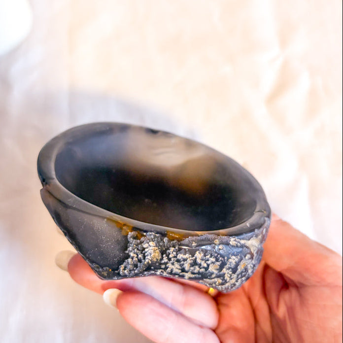 Hand holding a small black stone bowl against a neutral background