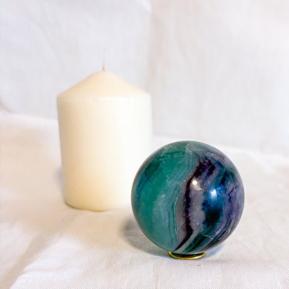 Fluorite green and purple crystal sphere  on a white surface with a white candle in the background